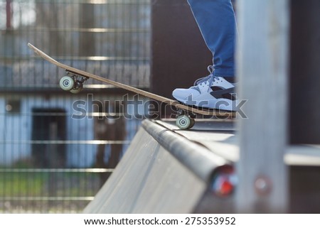 Close-up of skater\'s leg on a skateboard at the edge of a skate ramp preparing for a jump