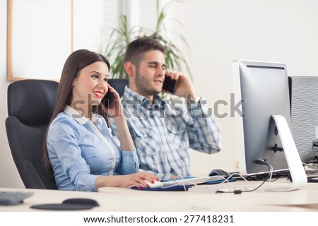 Two young business people talking on mobile phones while working in office