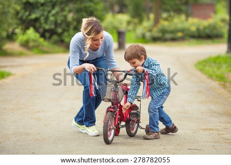Cute little boy and his mother playing with bicycle in a park