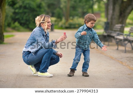 Cute little boy playing with his mother outdoors trying to catch soap bubbles