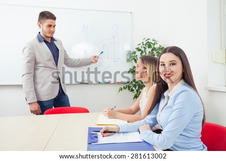 Young business team on a meeting in a conference room. Pretty young woman looking at camera and smiling, while young man explaining something to other woman in the background.