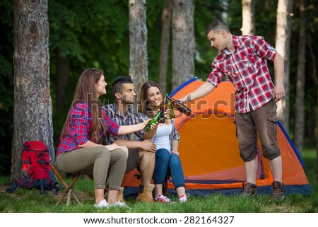 Group of cheerful young friends camping in forest and toasting with beer
