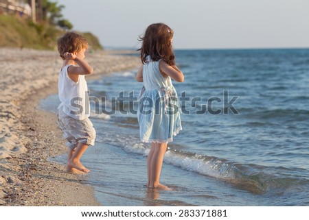Little girl and her little brother playing on the beach throwing stones to the water