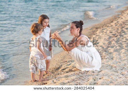 Mother educating her children about sea animals showing seashells to them while playing on the beach