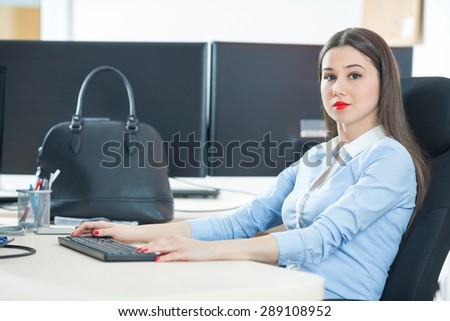 Portrait of smiling young businesswoman typing on computer keyboard and looking at camera