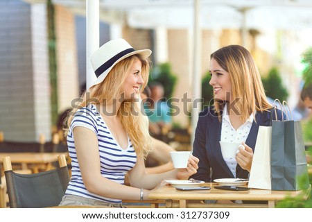 Two young girlfriends sitting in a cafe drinking coffee and chatting after shopping
