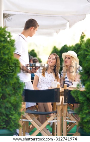Waiter taking an order from the two girls sitting in cafe