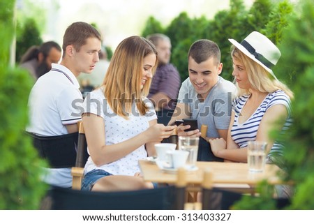 Young man and woman exchanging phone numbers while sitting with friends in a cafe