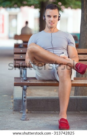Young man sitting on the park bench listening to music on his smart phone