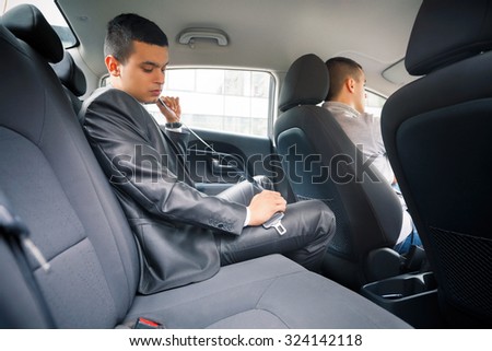 Young businessman tying belt in the back seat of the car
