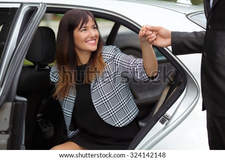 Chauffeur helping young business woman to get out from a luxury car