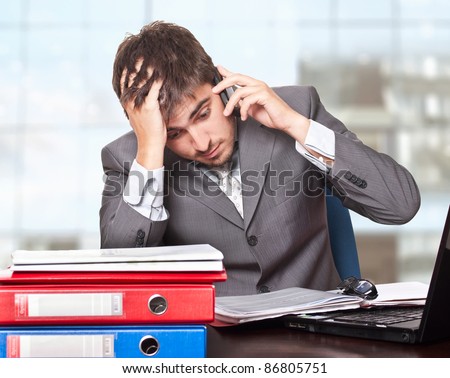 Young and tired business man talking on the phone on his desk
