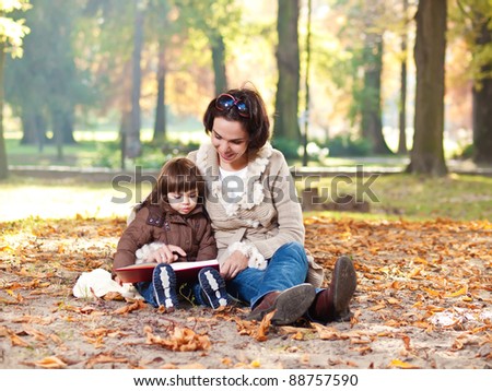 Mother and little daughter reading outdoors on a nice autumn day