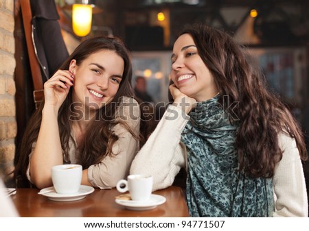 Two beautiful cheerful female friends in a cafe bar