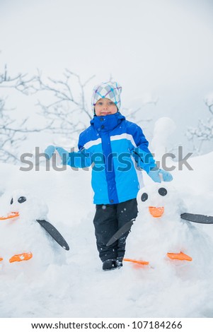 Smiling happy boy having fun outdoors on snowing winter day in Alps playing in snow.