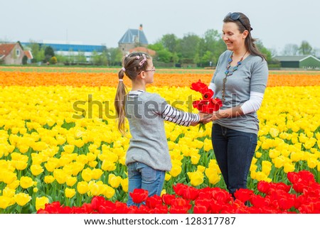 Girl and her mother with bouquet between of the yellow-red tulips field