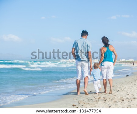 Back view of happy young family - mother, father and son having fun on the beach