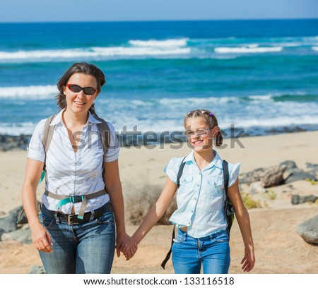 Mother with her daughter walking on a beach, wearing jeans and white shirts