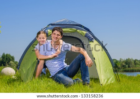 Father with his daughter resting on the grass and camping with tent