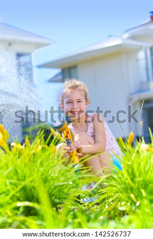 Little gardener girl watering flowers on the lawn near cottage. Vertical view