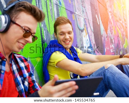 Happy teens boy with his friend by painted wall sunrise listening to music.