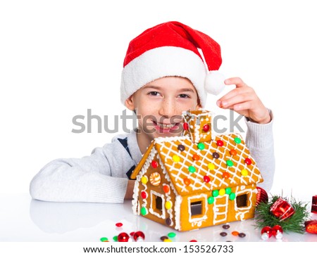 Christmas theme - Smiling boy in Santa\'s hat with gingerbread house, isolated on white