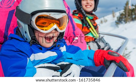 Portrait of happy girl in ski goggles and a helmet with his sister on the ski lift