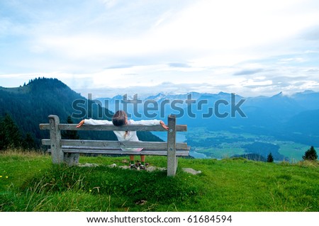 Activities at the top. Sweet girl sitting on a bench and looked at the panorama of mountains. Austria