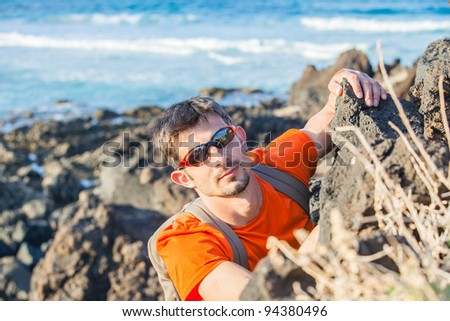 Young man in glasses with backpack climbing indoor wall. Backround sea