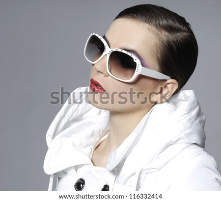 fashion model in sunglasses with white cost posing on gray background