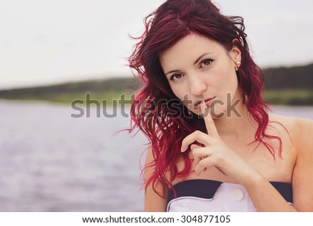 Secret woman.  Female showing hand silence sign, natural outdoor background