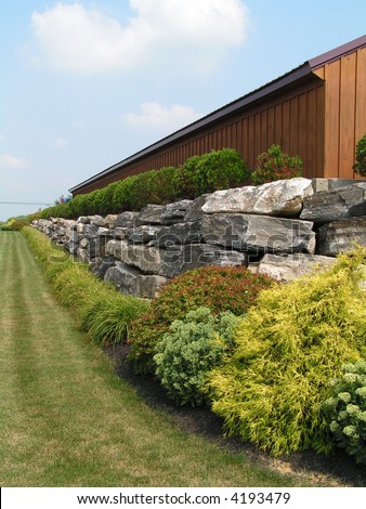 Boulder retaining wall at a commercial site with attractive plantings that include perennials, grasses and deciduous and evergreen shrubs
