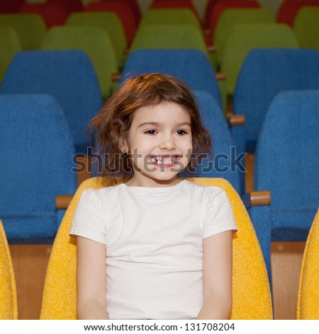 cute pretty smiling little girl sitting in the cinema hall