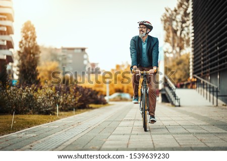 A handsome casual middle-aged businessman is going to the office by bicycle. He is driving bike in front of office district. Imagine de stoc © 