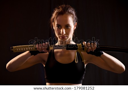Young Woman Holding Samurai Sword on Black Background.