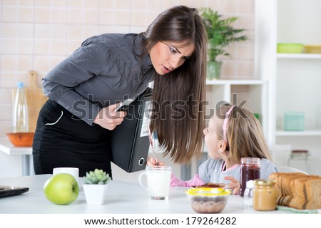Overworked Mother Rushing her little daughter in the morning to go faster because she late for work. Daughter having breakfast. Mother and Daughter getting angry with each other because of stress.