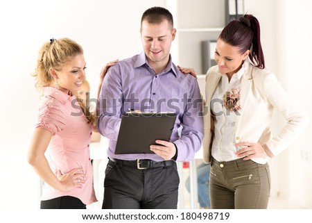 Three smiling co-workers standing in the office and discussing interesting question.