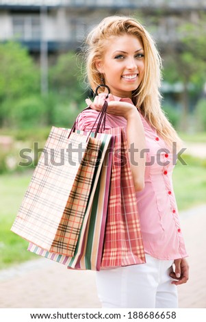 Portrait of beautiful smiling girl with shopping bags in the park. Looking at camera.