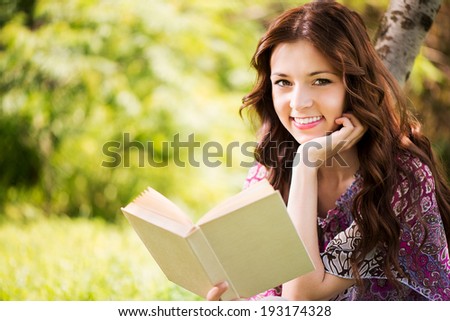 Beautiful Girl with a book in the park sitting on the grass and Expressing Positivity.