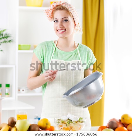 Beautiful young woman preparing fruit salad with Whipped Cream in a kitchen. Looking at camera.