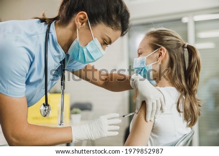 Nurse giving the Covid-19 vaccine to a cute teenager girl due to pandemic.
