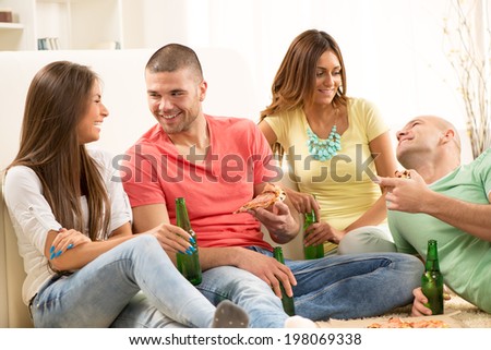 Friends enjoying eating pizza and drink a beer together at home party.