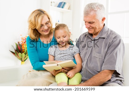 Grandparents with little girl reading book at home