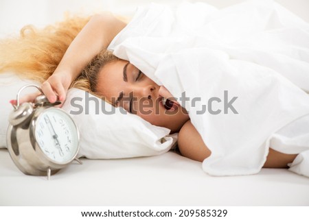Young woman lying in bed in the morning. She is waking up with alarm clock.