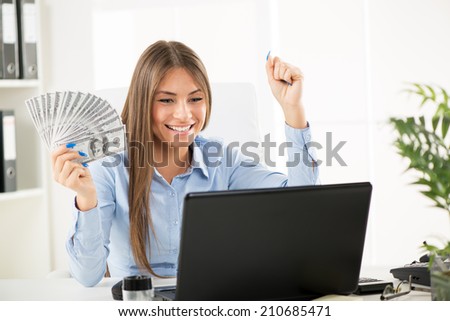 Happy successful Businesswoman in the office holding money with raised arms.