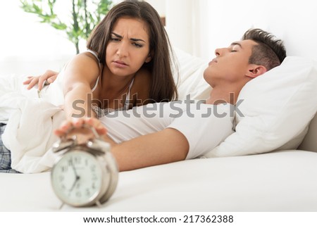 Beautiful Young couple sleeping in bed in the morning. Sleepy Girlfriends waking up with alarm clock.