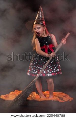 Little halloween witch in dark clothing with broom.