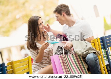 Young couple in the break after shopping at outdoor cafe watching the things they bought.