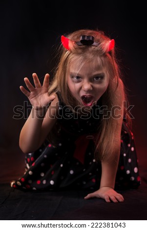 Little halloween witch in dark clothing with evil face wearing devil horns.