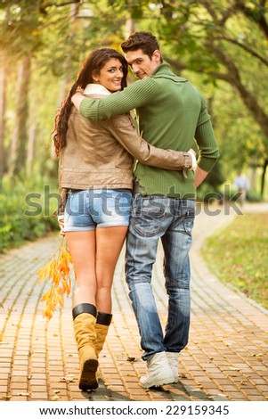 Young couple in love embraced walking on trails in the park looking behind at the camera with a smile on their faces.